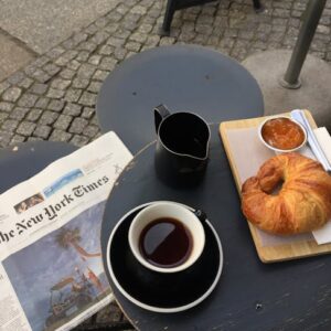 A cozy setup in Berlin featuring coffee, croissant, jam, and a newspaper on a cafe table.