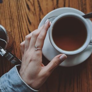 Hand with silver ring holding a coffee cup on a wooden table, captured from above.