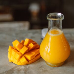 Sliced mango and fresh juice in glass carafe on rustic table.