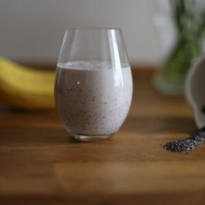 Glass of chia seed smoothie with banana and spilled seeds on wooden table.