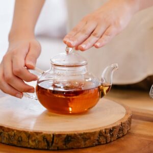 A close-up view of hands preparing herbal tea in a glass kettle. Warm and inviting.