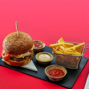 Tasty burger and fries with various dips on a vibrant red background.