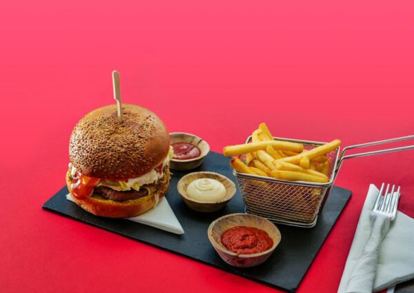 Tasty burger and fries with various dips on a vibrant red background.
