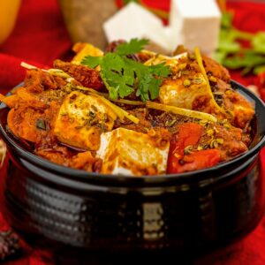 Spicy paneer tikka masala garnished with cilantro and spices on a vibrant red background.