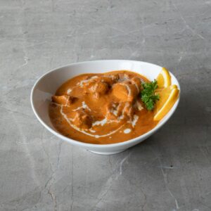 A savory bowl of butter chicken garnished with fresh herbs and citrus slices.